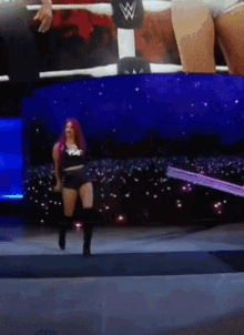 a woman with red hair is walking on a stage in front of a wrestling ring with a w on it