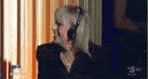 a woman wearing headphones and a cross necklace is smiling on a tv show