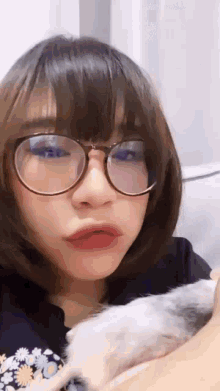 a girl wearing glasses is holding a small white hamster in her arms .