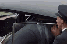 a man in a suit is getting out of a car while a man in a hat looks on .