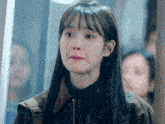 a woman with long black hair and bangs is wearing a brown jacket