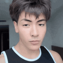 a close up of a young man 's face wearing a black tank top and looking at the camera .