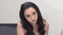 a woman with long black hair and a necklace is sitting on a couch .