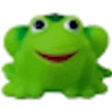 a green toy frog with a smile on its face is sitting on a white surface .