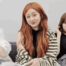 a woman with long red hair is wearing a striped shirt and sitting on a couch .