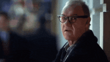 an older man wearing glasses and a scarf looks at the camera