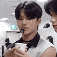 a man wearing a microphone and a choker is holding a cup .