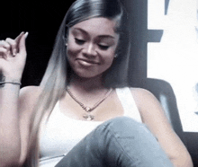 a woman in a white tank top and jeans is sitting on a couch with her legs crossed .