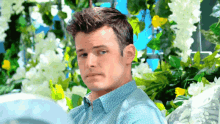 a man in a blue shirt is sitting in front of a bunch of flowers
