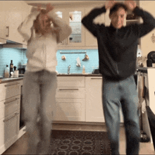 a man and a woman are dancing in a kitchen with their arms in the air