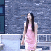 the woman is wearing a pink dress and standing in front of a brick wall .