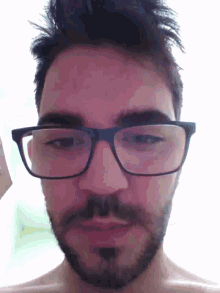 a man with glasses and a beard looks at the camera with his eyes closed