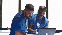 two men are looking at a laptop together .
