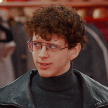 a young man with curly hair wearing glasses and a black turtleneck