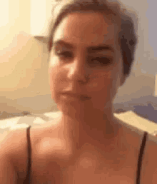 a woman in a black tank top is making a funny face while sitting on a bed .