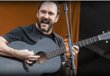 a man with a beard is singing into a microphone while playing a guitar