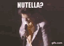 a man in a suit is singing into a microphone with the words `` nutella ? '' written above him .