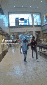 two men are walking in a mall with tiktok written on the bottom right
