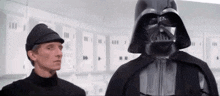 darth vader is standing next to a man in a black hat .