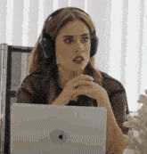 a woman wearing headphones is sitting at a desk with a laptop .