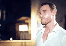 a man with a beard and a white shirt is standing in front of a building at night .