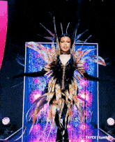 a drag queen is standing on a stage with her arms outstretched in front of a pink and blue curtain ..