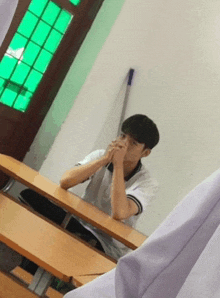 a young boy sits at a desk with his hands folded