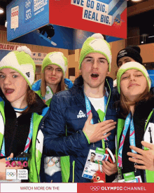 a group of young people are posing for a photo in front of an olympic channel advertisement