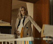 a pregnant woman in a plaid coat is standing in front of a crib holding her belly .