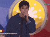 a man in a denim jacket sings into a microphone in front of a flag