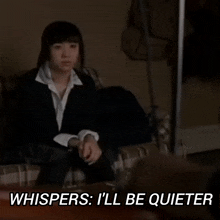 a woman in a suit sits on a couch with the words whispers i 'll be quieter above her