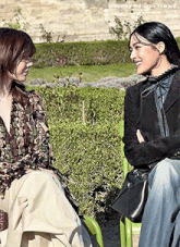 two women are sitting on a green bench talking to each other .