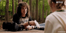 a man with long curly hair is sitting at a picnic table with a woman and talking to her .