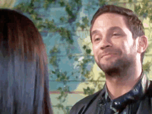 a man in a leather jacket looks at a woman in a blue shirt