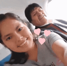 a man and a woman are posing for a picture with pink hearts surrounding them