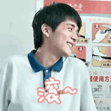 a young man wearing a white shirt with a blue collar is smiling in front of a poster with chinese writing on it