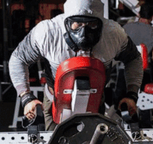 a man wearing a mask and a hood is lifting weights in a gym .