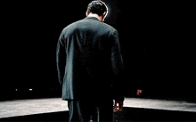 a man in a suit is standing on a stage with his arms outstretched in front of a crowd .