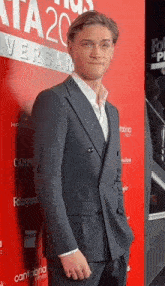 a man in a suit stands on a red carpet in front of a sign that says ' ata 20 versal '