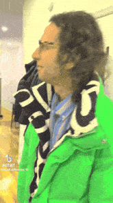 a man with curly hair wearing a green jacket and a scarf with the letter g on it