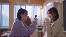 two girls are standing next to each other in a room and one is holding something in her hand .