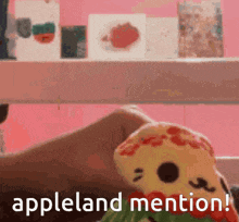 a stuffed animal is sitting in front of a pink wall with the words appleland mention written below it