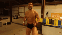 a man without a shirt is running in a room with a sign that says versatile bean on it