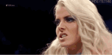 a woman with blonde hair and blue eyes is making a funny face in a wrestling match .