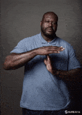 a man in a blue shirt has his hands folded in front of his face