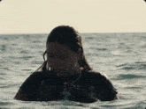 a woman in a black shirt with a bat on it is swimming in the ocean