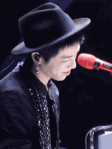 a man wearing a hat and ear buds holds his hand to his face in front of a microphone