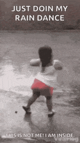 a little girl is dancing in the rain on a sidewalk .