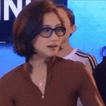 a woman wearing glasses and a brown shirt is standing in front of a sign that says n