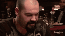 a man with a beard is sitting at a table with a travel hd logo on the bottom .